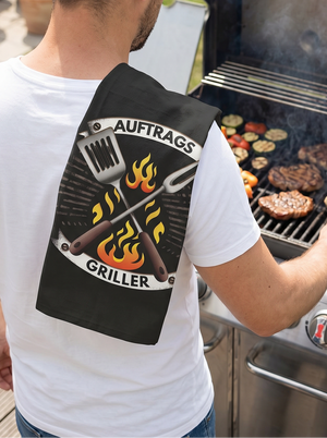 Mann am Grill mit Geschirrtuch „AuftragsGriller“ von CALEO d.sign – humorvolles BBQ Design für Grillfans und Grillmeister