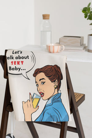 Geschirrtuch „Let’s talk about Sekt Baby“ als stilvolle Küchendeko mit humorvollem Sekt Statement über eine Stuhllehne gehängt